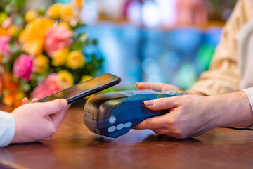 Shopper hands with phone making contactless payment using nfc technology at checkout terminal in flower shop