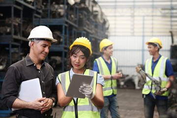 Industrial engineer worker woman and man wearing helmet discussing and working together with laptop computor and digital tablet at manufacturing plant factory, young people working in industry