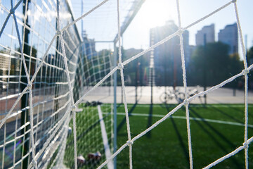 White soccer goal net on a sunny day. Empty artificial football field before match. Closeup blurred photo.