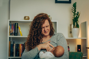 Mother in pain breastfeeding baby - obrazy, fototapety, plakaty