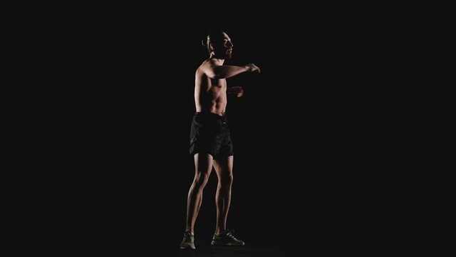 An athletic man does a warm-up on a black background. Slow motion