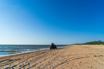 The guy and the girl ride a quad bike along the sandy seashore.