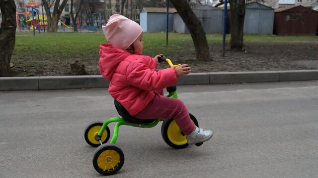 Toddler girl who rides a tricycle down the street. Side view.