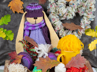 The knitted purple toy hare sits in tangles of threads and autumns.