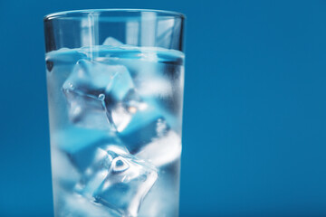 Ice cubes in a glass with crystal clear water on a blue background.