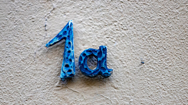 1a, metal sing in blue on a wall, small spider close to the number