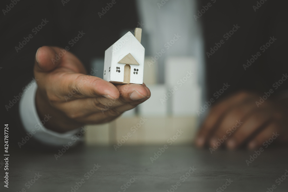 Poster Realtors in suit holding mini wood house model. The concept of selling a home.