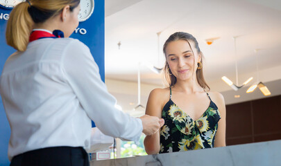 Fototapeta na wymiar Young travellers standing at reception desk with female receptionist standing at hotel counter, Happy guest and receptionist at hotel reception