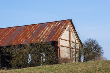 Obraz premium old abandoned barn with a roof made of rusty metal iron and a brick wall