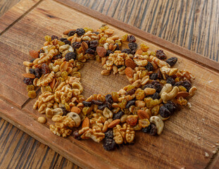 Mix of nuts and dried fruits grouped on a wooden board. In the middle a heart shape. Raisins, cashews, almonds, walnuts, peanuts.