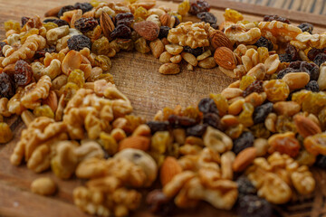 Mixed dried fruits and nuts grouped together. In the middle a heart shape with wood texture. Raisins, cashews, almonds, walnuts, peanuts.