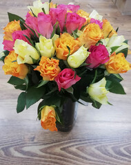 Bouquet of multicolored roses in transparent vase put on wooden table. Spring background, flower wallpaper.