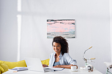 African american freelancer smiling at camera near gadgets and cup on table