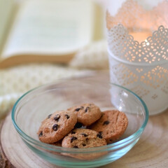 Bowl of chocolate chip cookies, lit candle and open book on a bed. Selective focus.