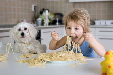 Little blond boy, toddler child, eating spaghetti for lunch and making a mess at home in kitchen