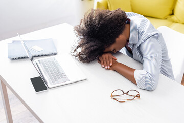 Tired african american freelancer sitting near devices and eyeglasses on table