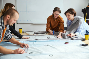 Woman tailor showing fabric sheet to co-worker while cutting