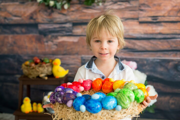 Beautiful blond child, toddler boy, painting easter eggs with mother at home, making easter wreath