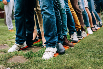  Team building event. Colleagues stand next to each other on wooden skis. Their legs are tied. Team...