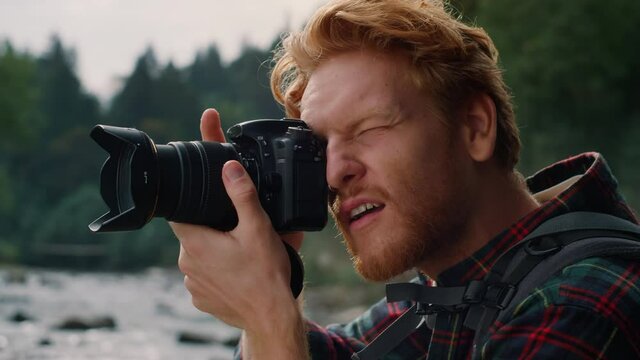 Redhead man with digital camera taking pictures of green landscape