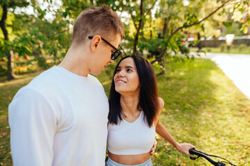 Lovely couple is standing in the park, smiling, looking at each other with enjoyment and passion,...