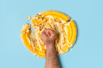 Diet concept with a man fist smashing a cake, top view.