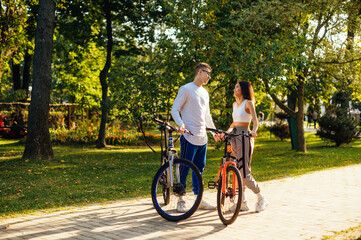 Two people, male and female are having a date in the city park and riding their colorful bicycles. Young stylish couple is holding hands and smiling.