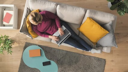 woman lying on couch typing on laptop computer top down view,,comfortable female resting on sofa wearing casual clothing using notebook writing email works from home high angle shot Vertical 9 16 - Powered by Adobe