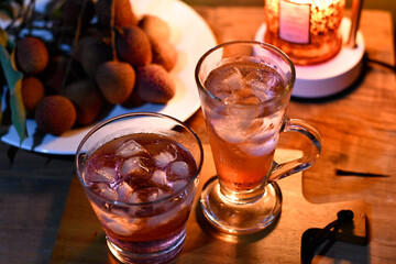 Glass of lychee drink, fruit beverage on wooden counter bar with bunch of fresh lychee background. Concept for cocktails preparation,  sparkling wine and alcohol that mixed with fruit juice. 