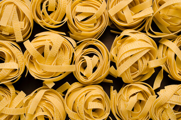 Fettuccine Tagliatelle pasta on grey background. Spaghetti nests. Yellow pasta.Uncooked ingredient for traditional Italian cuisine.Top view