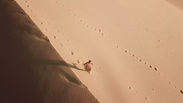 Aerial view of man running along the large sand dunes. Drone point view of a young man running in the desert at sunrise.