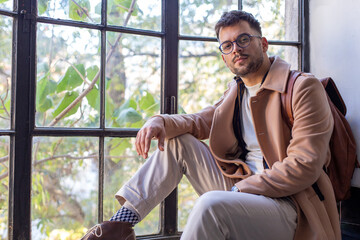 Portrait of the young male student sitting by the window.