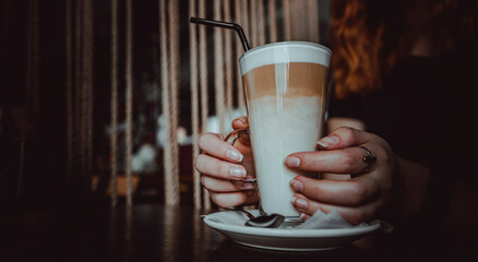 Female hands hold a glass of flat white coffee in caffee