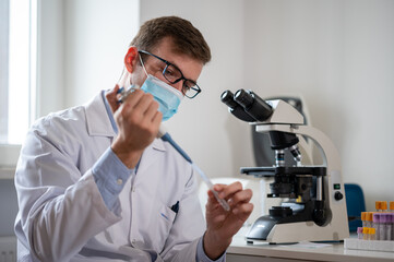 Male scientist working in a laboratory and looking through the microscope, examining samples.	