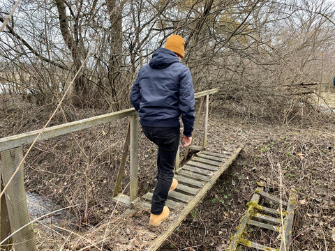 A man crosses over a wooden bridge. Rural bridge over the moat. Walk along the wooden bridge.