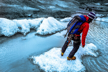 Young mountain guide man with crampons, blue backpack, red jacket and a wool hat leads the way during an adventorous glacier trip for tourists in Vatnajökull national park Iceland