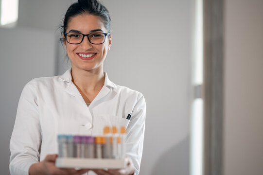 Portrait of smiling woman laborant holding test tubes in laboratory.