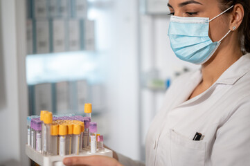 Portrait of smiling woman laborant eith face mask holding test tubes in laboratory.