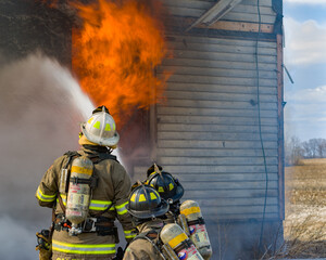 Firefighters in action spraying water on a home that is on fire as part of a training exercise.