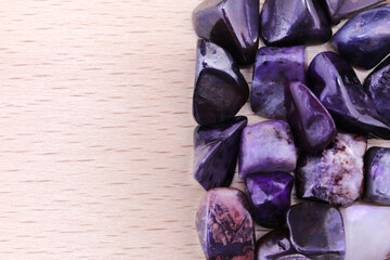 Sugilite heap jewel stones on half light varnished wood texture. Pile mineral pebbles background. Place for text.