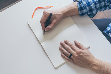 man writing in notebook with fountain pen on white table