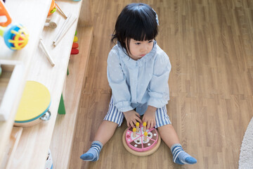 A toddler girl is playing a wooden toy cake. - 424819502