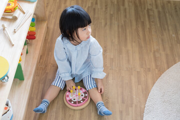 A toddler girl is playing a wooden toy cake. - 424819516