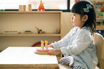 A toddler girl is playing a wooden toy cake. - 424819536