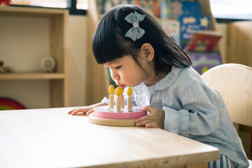 A toddler girl is blowing a toy cake.