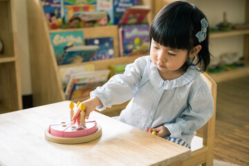A toddler girl is playing a wooden toy cake.