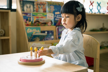 A toddler girl is playing a wooden toy cake.