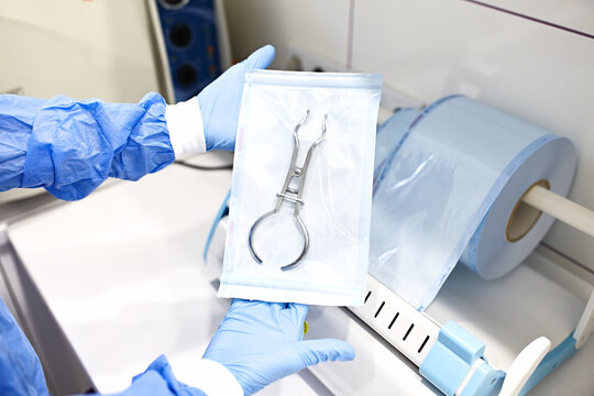 Sterilizing medical instruments in autoclave. Dental office. Close up dentist assistant's hands holding packaged with vacuum packing machine medical instruments ready for sterilizing in autoclave.