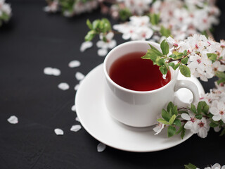 A cup of hot tea on a black table with branches of white cherry blossoms