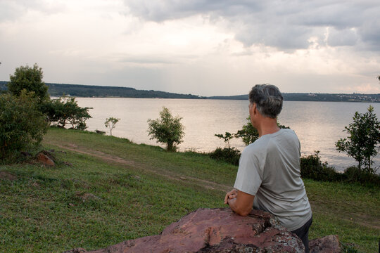 Senior man at Parque Das Gar&ccedil;as, in Brasilia, leaning on a big rock while looking over Lake Paranoa

